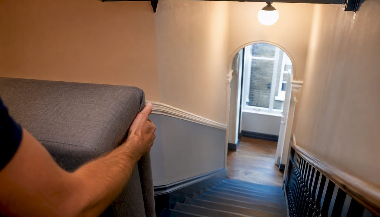 Mover carrying sofa up a narrow stairwell